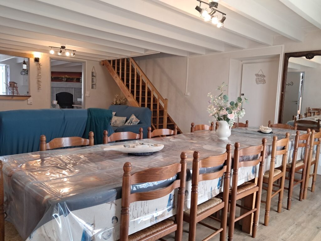 Séjour Gite "les p'tites cagouilles" Salle à manger rustique avec table dressée, chaises en bois, canapé bleu et cheminée en pierre