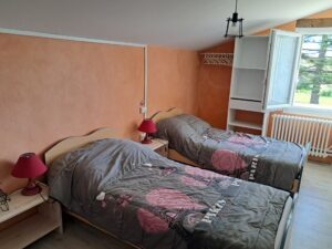 Chambre avec deux lits simples, lampes de chevet et vue sur les arbres par la fenêtre