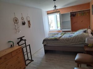 Chambre cosy avec lit fait, étagères murales décoratives, miroir sur pied et vue sur l'extérieur par la fenêtre