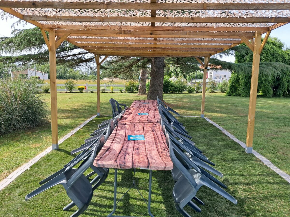Pergola en bois avec table en planches et bancs sous un auvent en parc