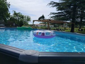 Piscine extérieure avec une bouée gonflable colorée et des transats sous une pergola en bois
